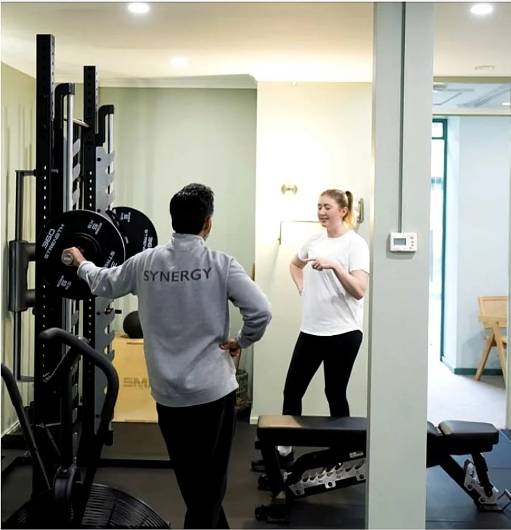 A Synergy coach talking through the session with a client at the squat rack, McKinnon