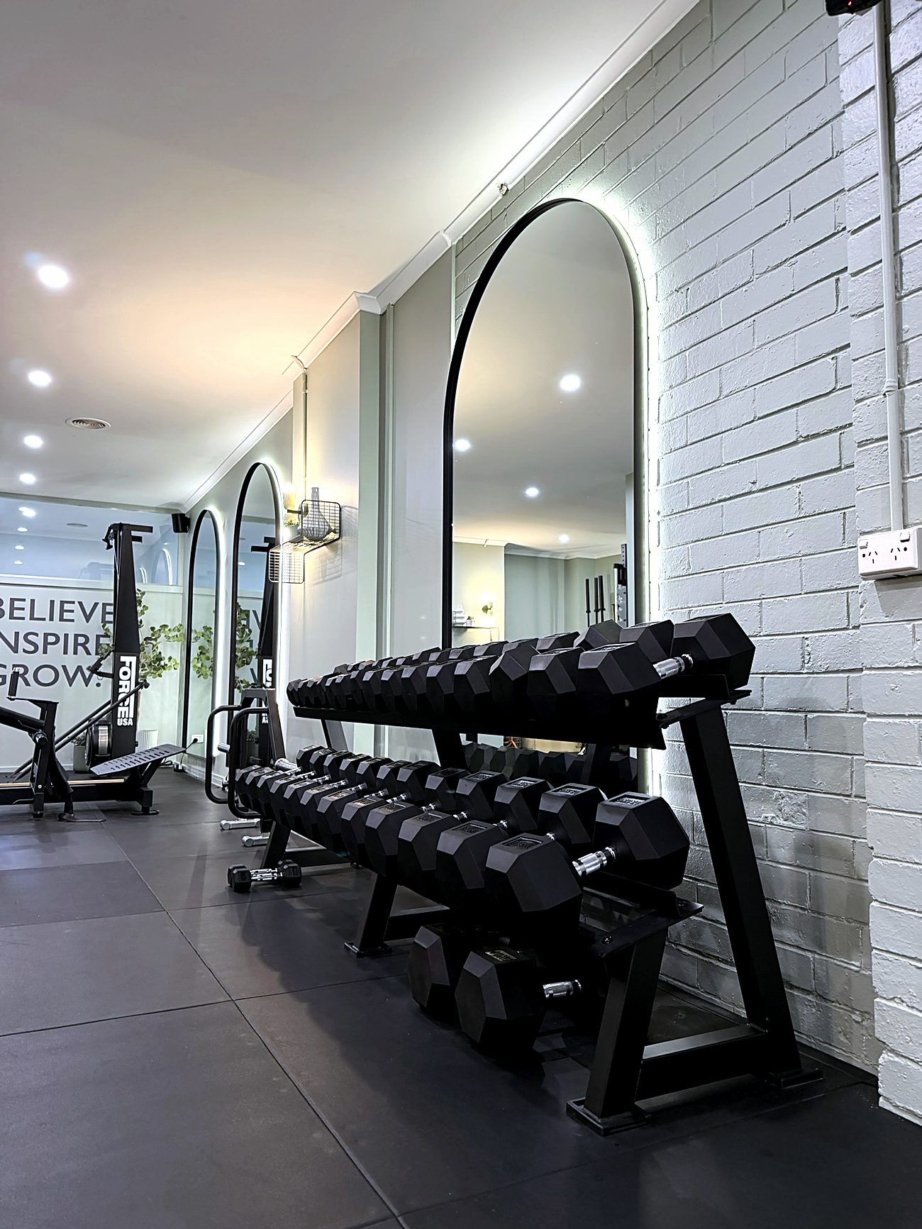 Arched mirrors and the dumbbell rack along the brick wall of the Synergy studio in McKinnon