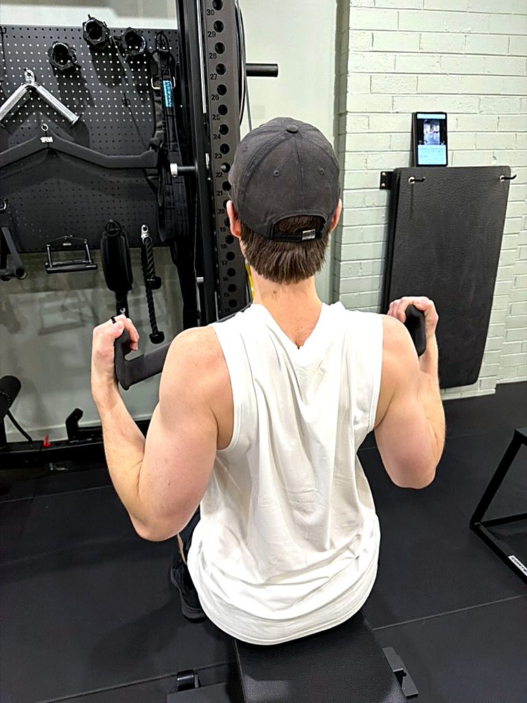 A client driving through the bottom of a coached pulldown rep at the studio rack