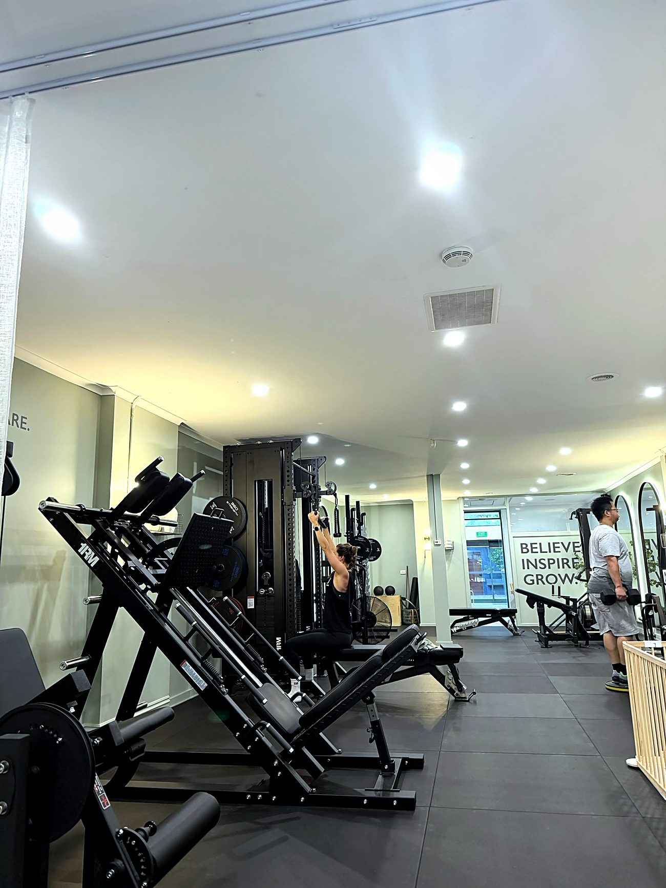 The length of the Synergy studio floor, with clients training at the rack and the free-weights end