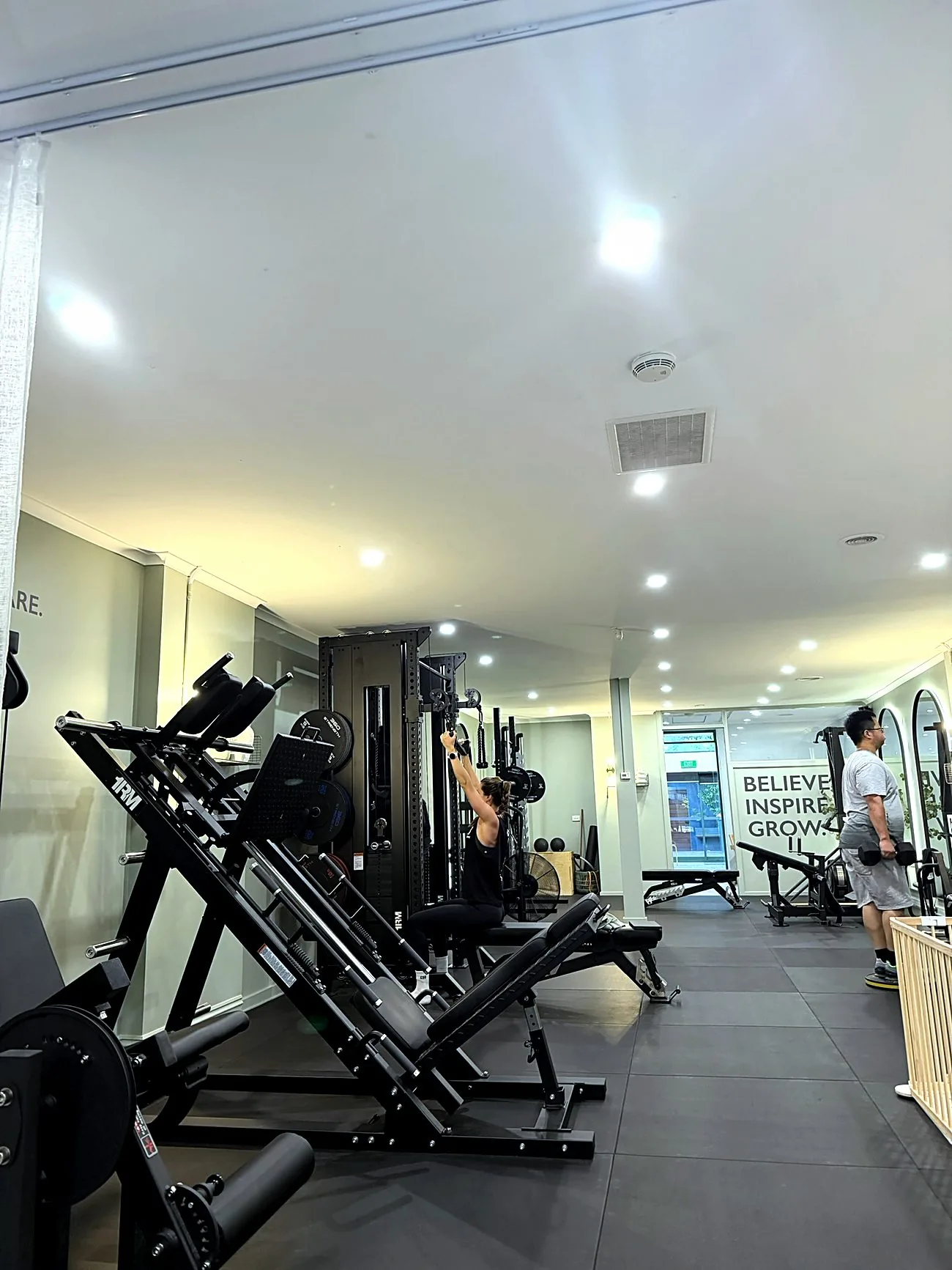 The length of the Synergy studio floor, with clients training at the rack and the free-weights end